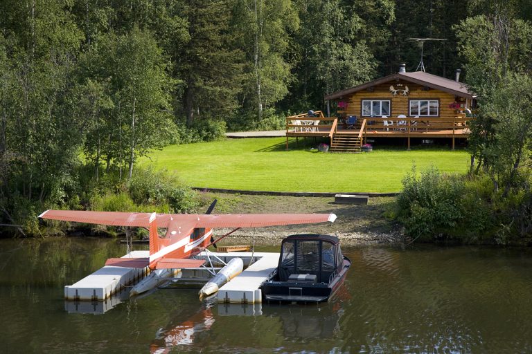 A log cabin with a floatplane and boat in the frontyard.