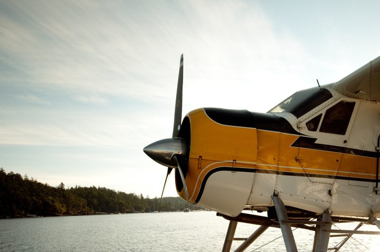 A passenger sea plane in Friday Harbor of the San Juan Islands. A windswept cloudy sky in the background with an evergreen tree shore line. The image has room for branding and messaging and has a retro look and feel